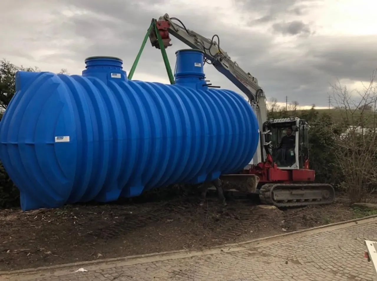 Citerne de récupération d'eau de pluie levée par une pelle mécanique avant enfouissement